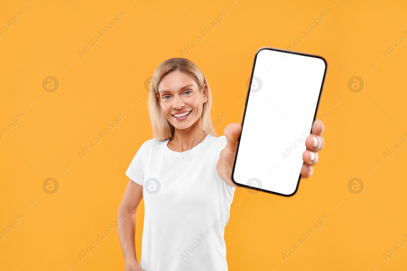 Photo of Happy woman holding smartphone with blank screen on orange background
