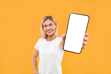 Happy woman holding smartphone with blank screen on orange background