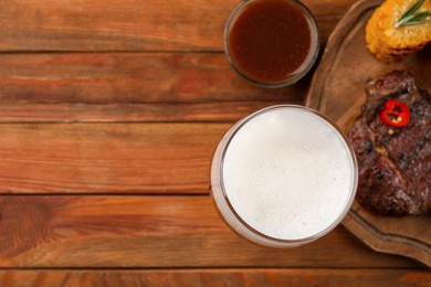 Photo of Glass of beer, delicious fried steak and sauce on wooden table, flat lay. Space for text