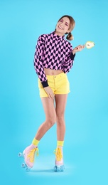 Young woman with lollipop and retro roller skates on color background