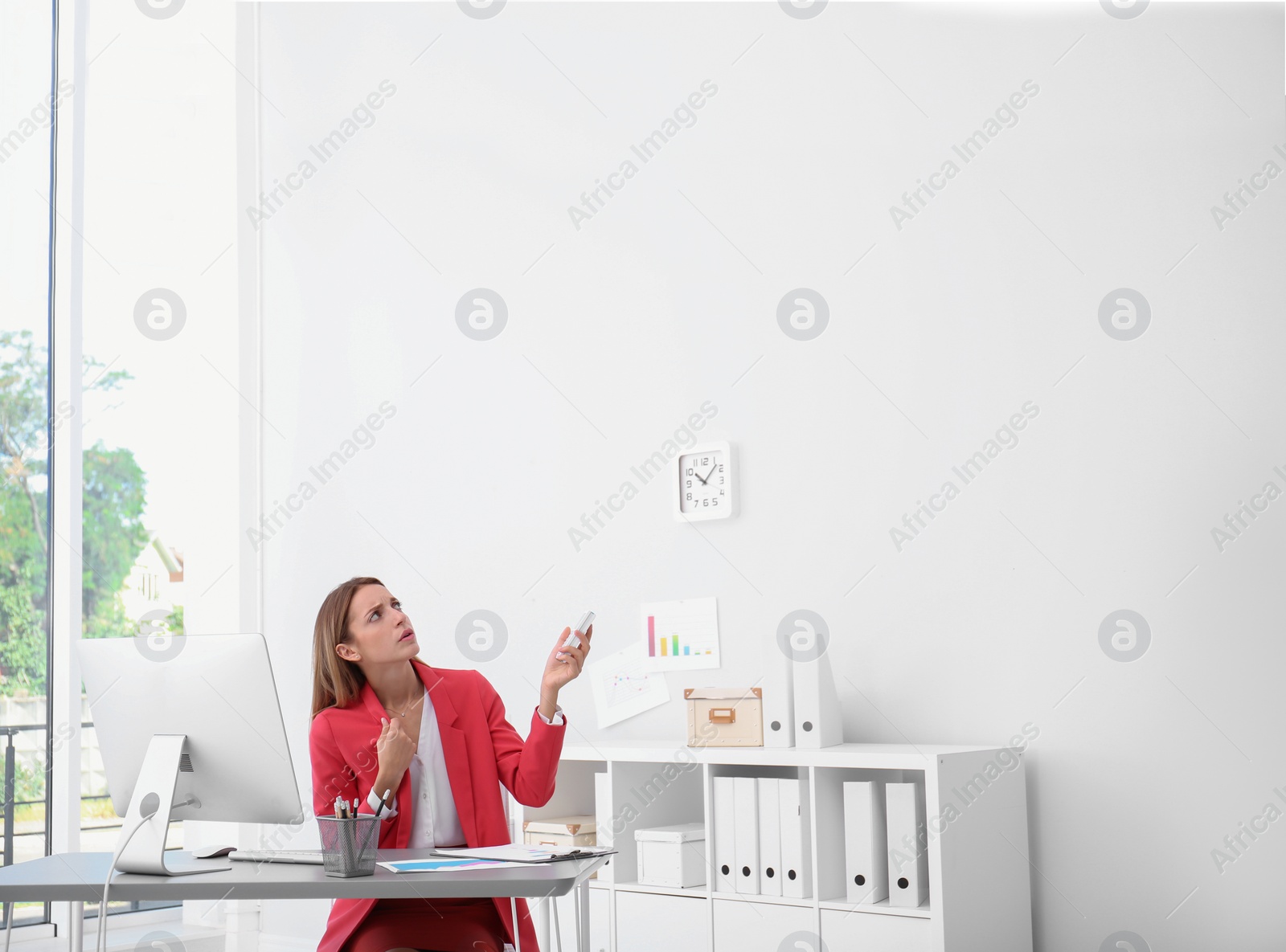 Photo of Young woman suffering from heat under broken air conditioner in office