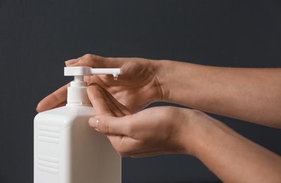 Woman applying hand sanitizer on grey background, closeup. Personal hygiene during COVID-19 pandemic