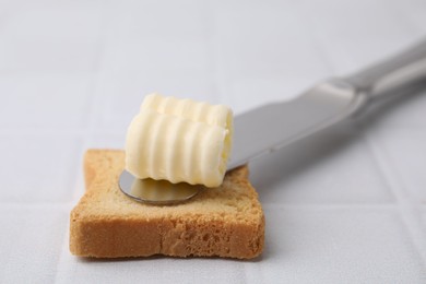 Photo of Tasty butter curl, knife and piece of dry bread on white tiled table, closeup