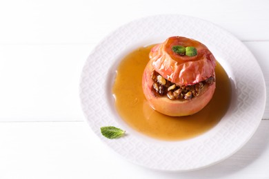 Photo of Tasty baked apple with nuts, honey and mint on white wooden table, closeup