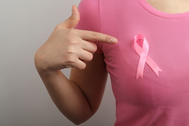 Photo of Woman with pink ribbon on grey background, closeup. Breast cancer awareness