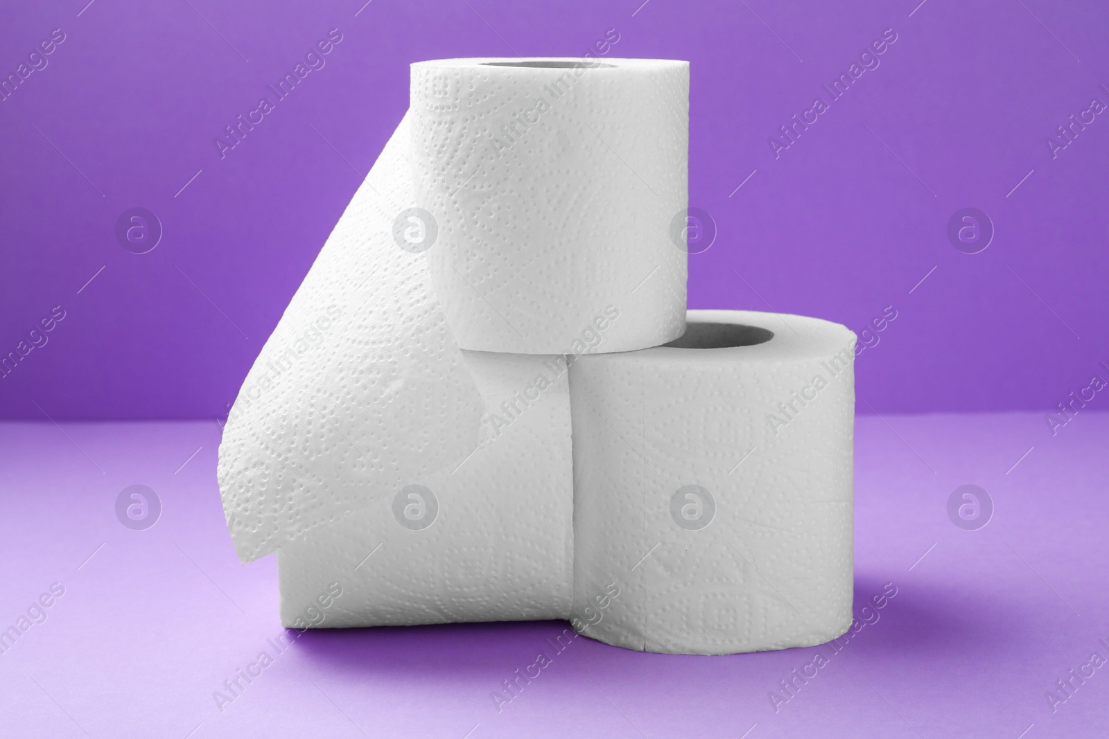 Photo of Soft toilet paper rolls on violet background, closeup