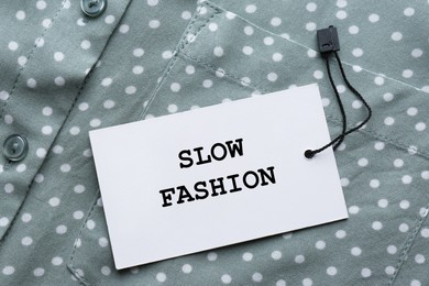 Image of Conscious consumption. Tag with words Slow Fashion on shirt, top view