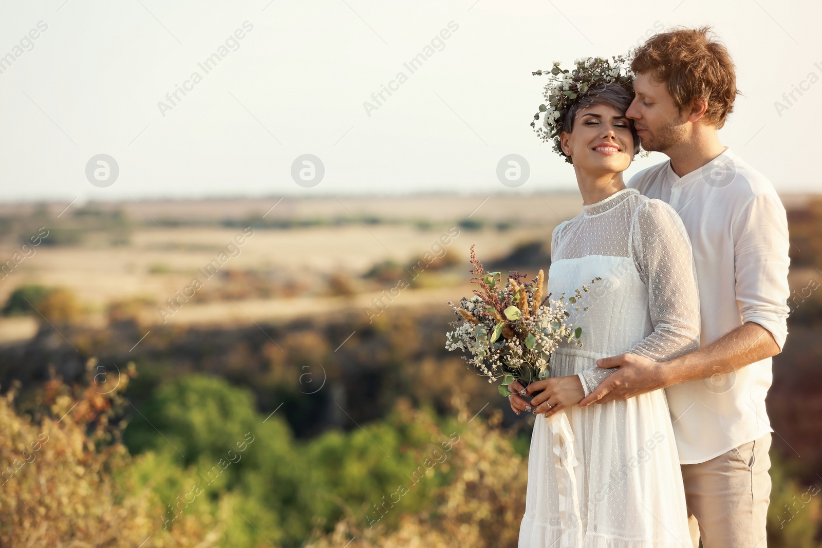 Photo of Happy newlyweds with beautiful field bouquet outdoors