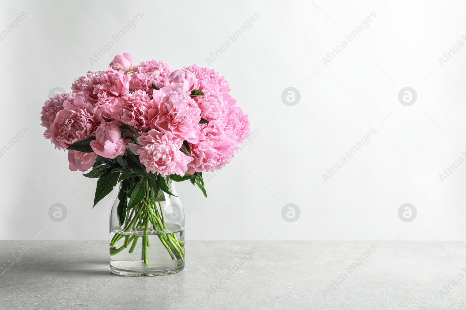 Photo of Vase with beautiful peony flowers on table against light background