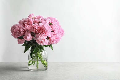 Vase with beautiful peony flowers on table against light background