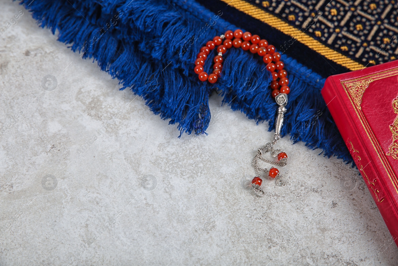 Photo of Muslim prayer beads, Quran, rug and space for text on grey background