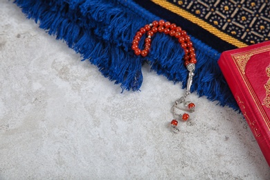 Muslim prayer beads, Quran, rug and space for text on grey background