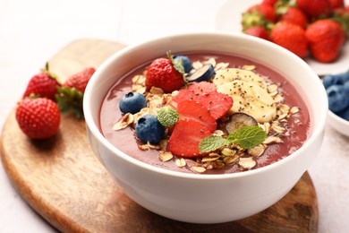 Photo of Delicious smoothie bowl with fresh berries, banana and granola on table, closeup