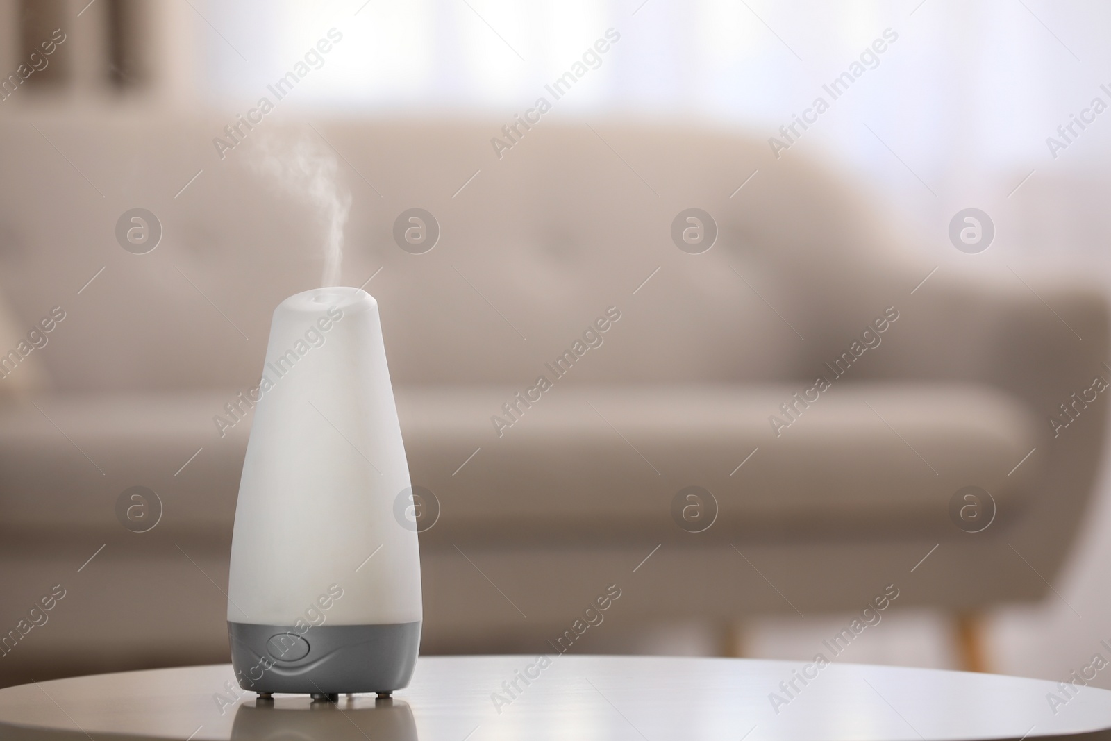 Photo of Modern essential oil diffuser on table indoors. Space for text