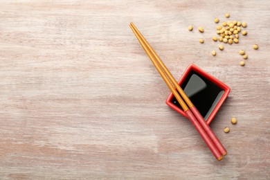 Soy sauce in bowl, soybeans and chopsticks on wooden table, flat lay. Space for text