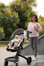 Young mother walking with her adorable baby in stroller outdoors