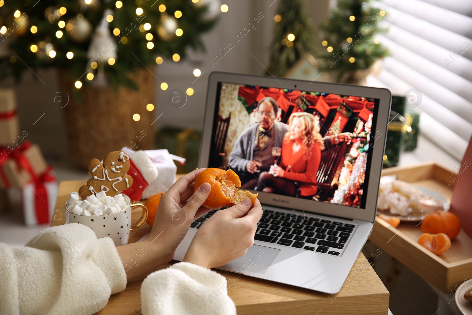 Photo of MYKOLAIV, UKRAINE - DECEMBER 25, 2020: Woman with tangerine watching Surviving Christmas movie on laptop at home, closeup. Cozy winter holidays atmosphere