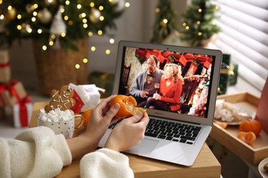 Photo of MYKOLAIV, UKRAINE - DECEMBER 25, 2020: Woman with tangerine watching Surviving Christmas movie on laptop at home, closeup. Cozy winter holidays atmosphere