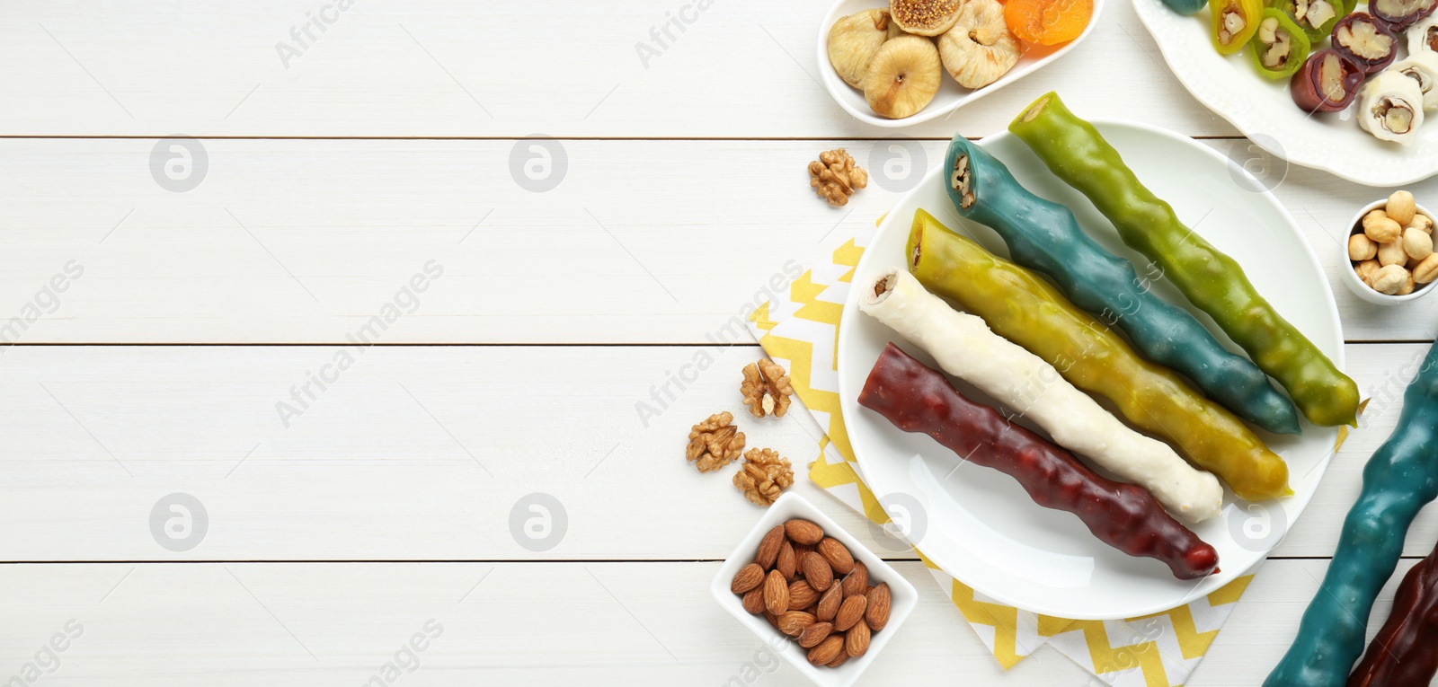 Photo of Delicious sweet churchkhelas and ingredients on white wooden table, flat lay. Space for text