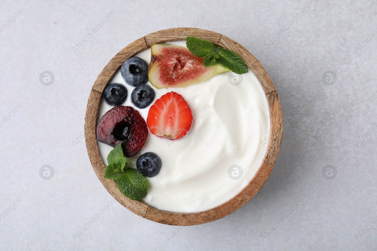 Photo of Bowl with yogurt, berries, fruits and mint on light grey table, top view