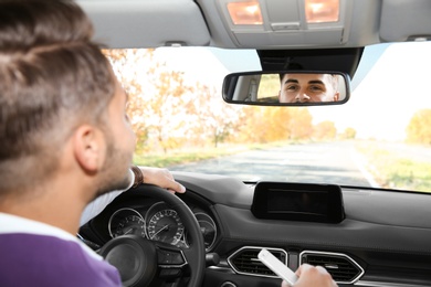 Young handsome man looking into interior mirror in car