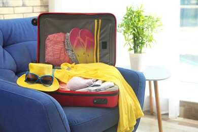 Photo of Open suitcase with different clothes and accessories for summer journey on armchair