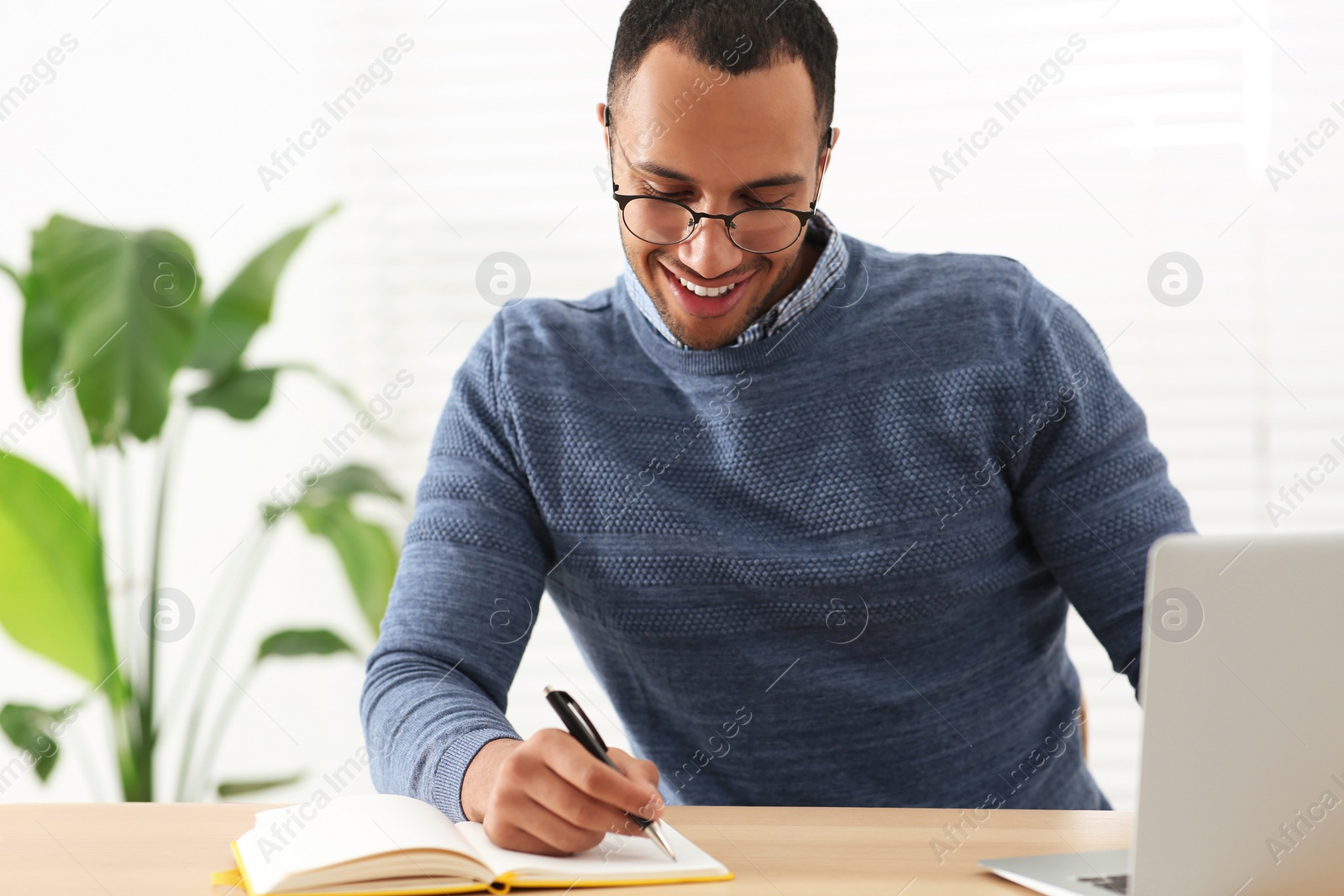 Photo of Smiling African American man writing in notebook at wooden table