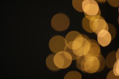 Blurred view of golden lights on black background, space for text. Bokeh effect