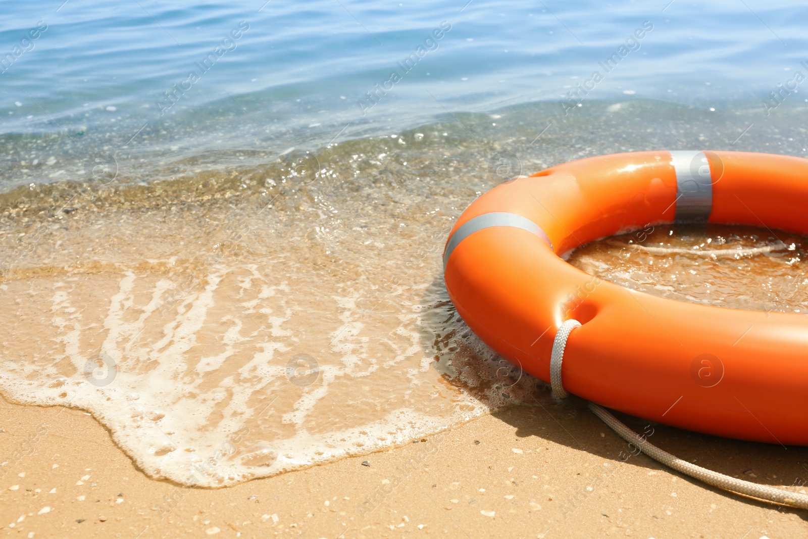 Photo of Orange life buoy on sand near sea, closeup. Emergency rescue equipment