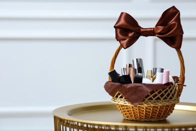 Photo of Gift set in wicker basket on golden table near white wall. Space for text