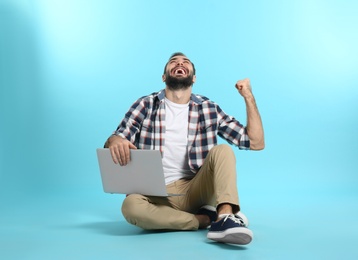 Emotional young man with laptop celebrating victory on color background