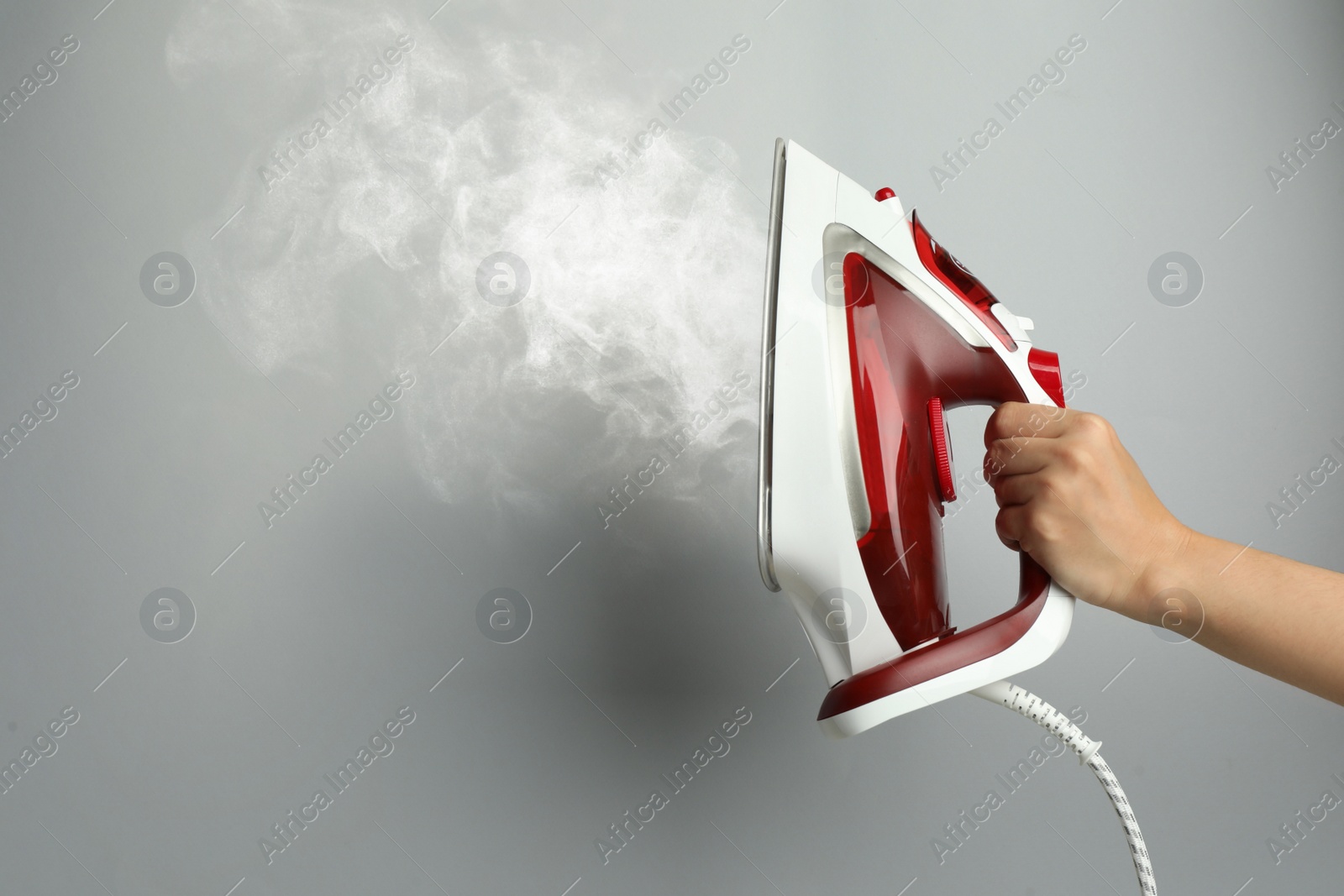 Image of Woman holding modern iron with steam on light grey background, closeup. Space for text