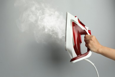 Image of Woman holding modern iron with steam on light grey background, closeup. Space for text