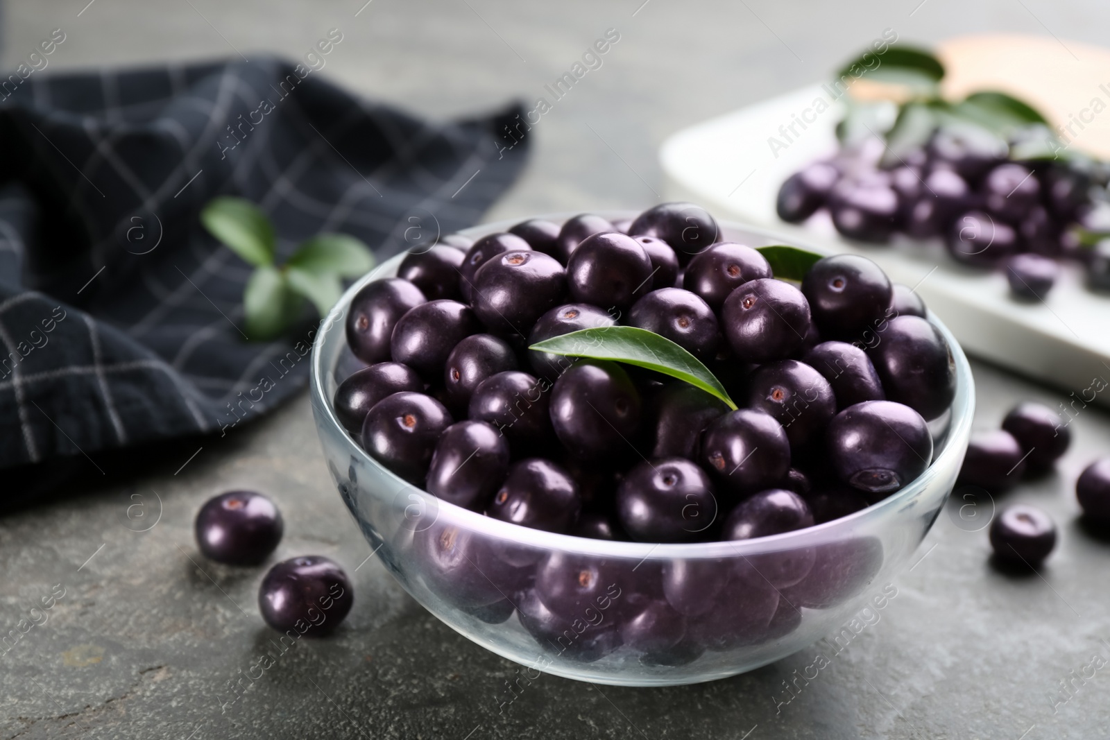 Photo of Fresh acai berries in glass bowl on grey table, closeup