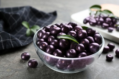 Fresh acai berries in glass bowl on grey table, closeup