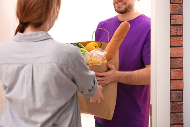 Photo of Courier giving paper bag with products to customer at home, closeup. Food delivery service