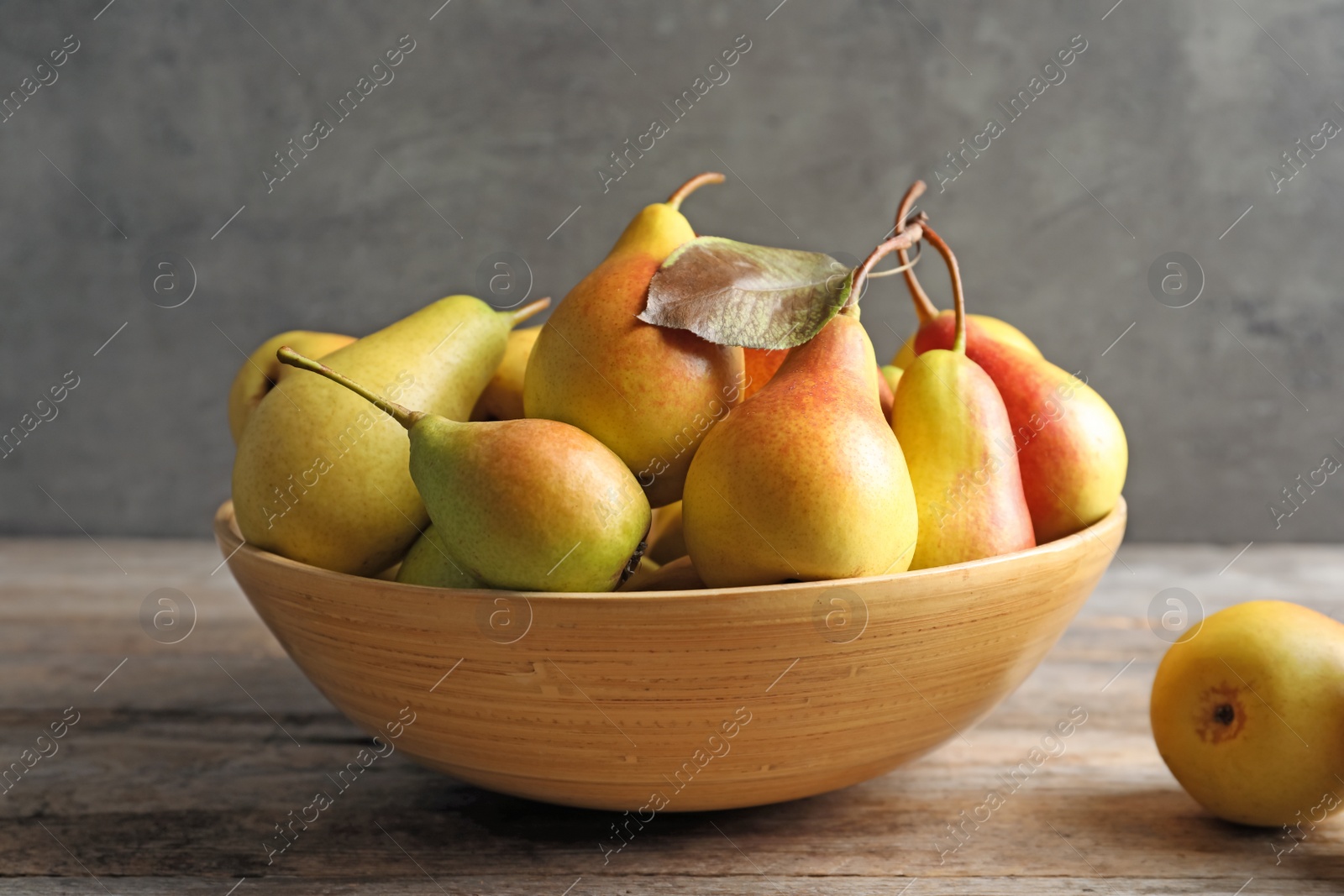 Photo of Bowl with ripe pears on table against grey background