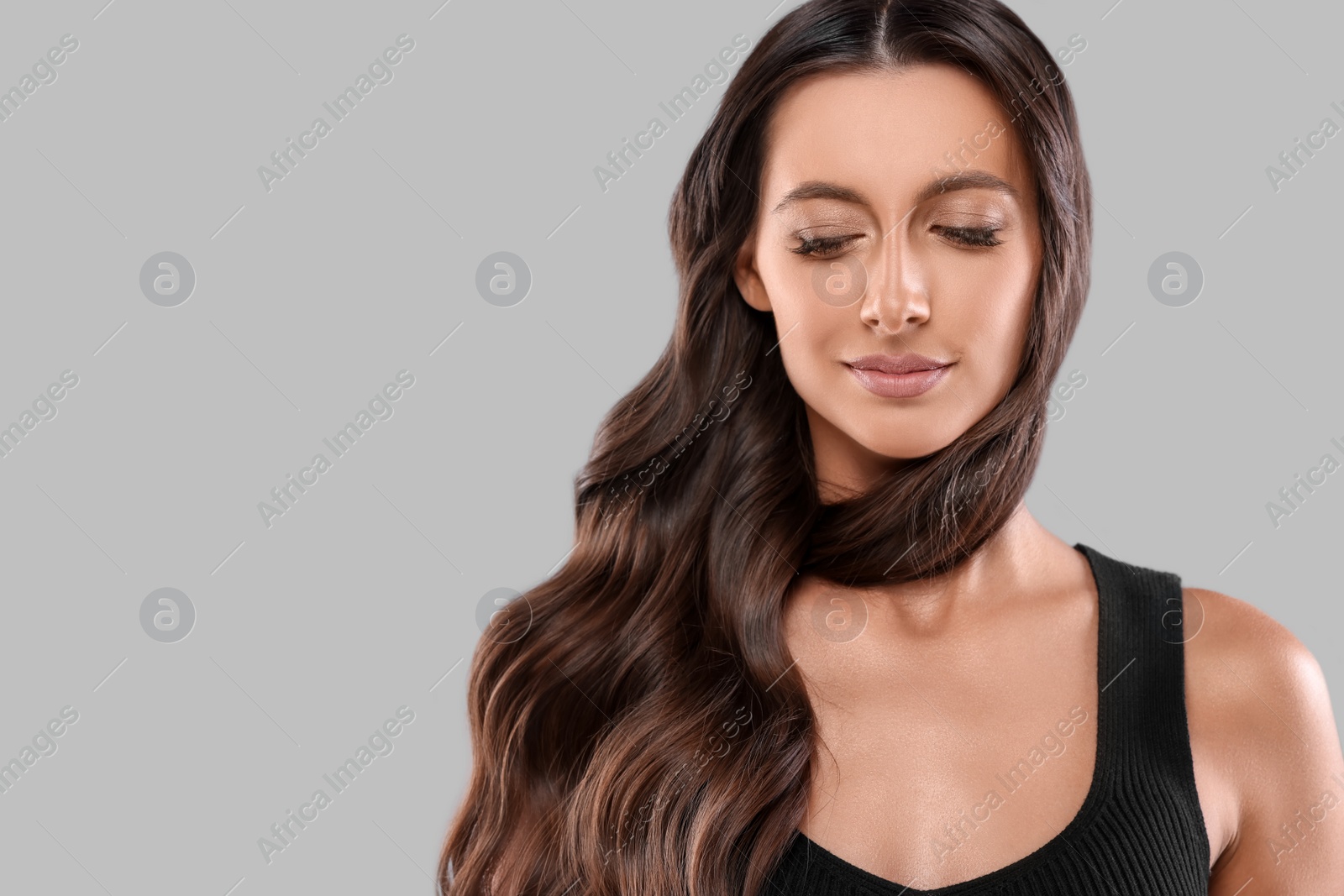 Photo of Hair styling. Beautiful woman with wavy long hair on grey background, space for text