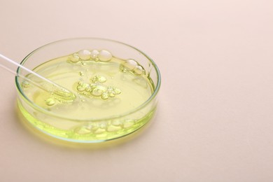 Photo of Petri dish with color liquid sample and pipette on beige background, closeup. Space for text