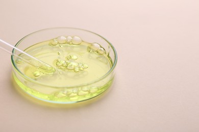 Petri dish with color liquid sample and pipette on beige background, closeup. Space for text