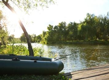 Inflatable boat with rod for fishing near wooden pier at riverside