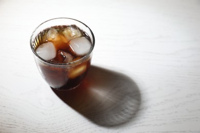 Photo of Refreshing iced coffee in glass on white wooden table. Space for text