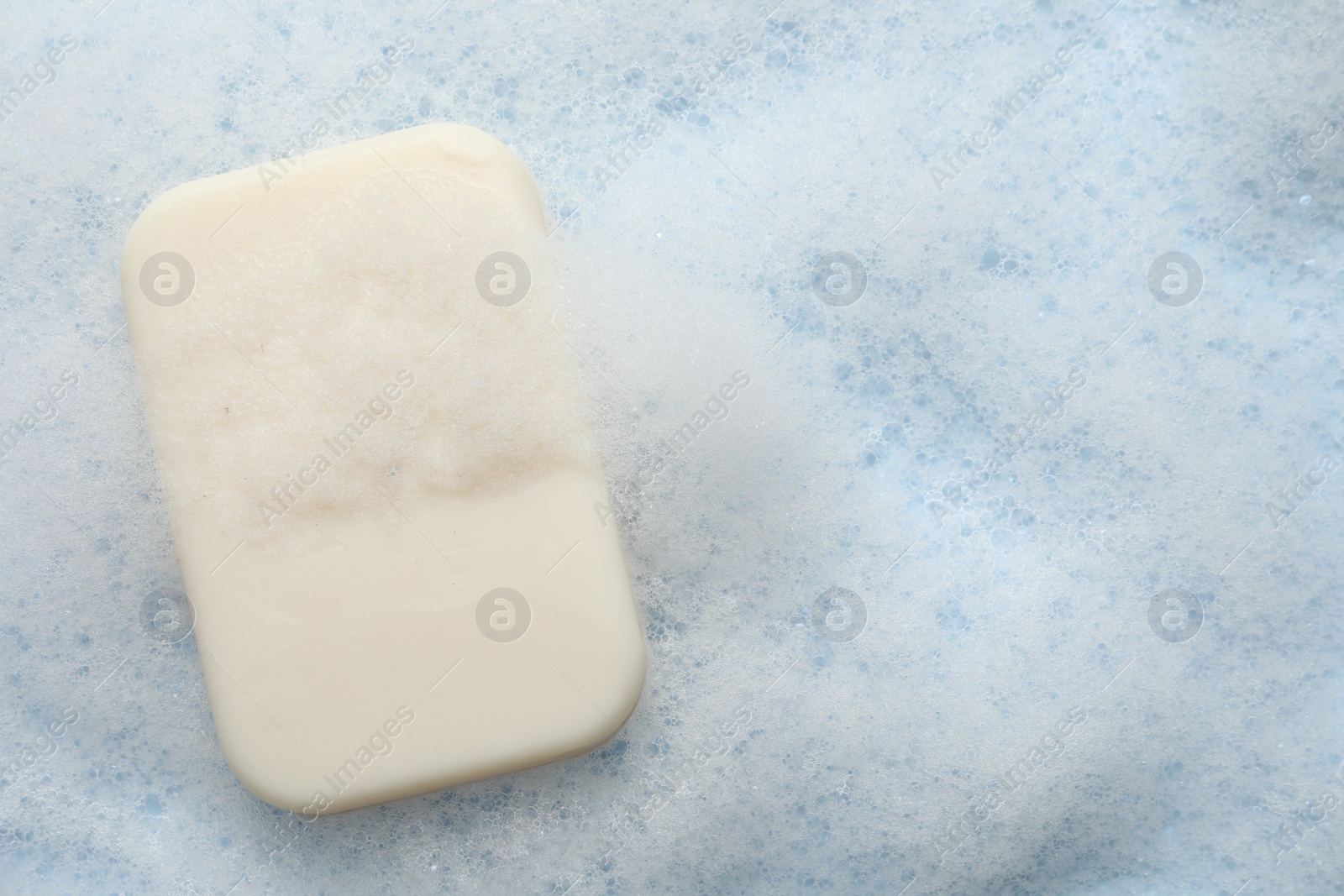 Photo of Soap with fluffy foam on light blue background, top view. Space for text