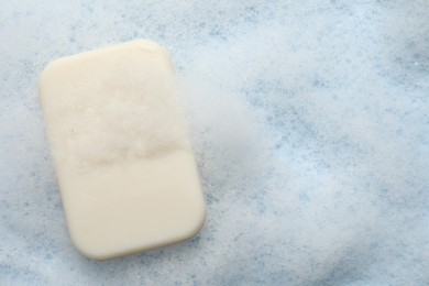 Soap with fluffy foam on light blue background, top view. Space for text