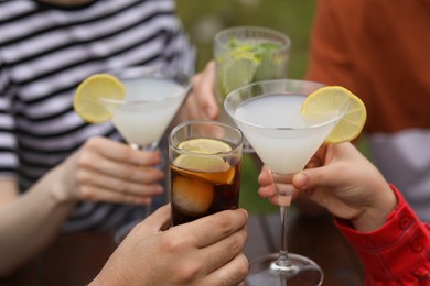 Friends clinking glasses with cocktails outdoors, closeup