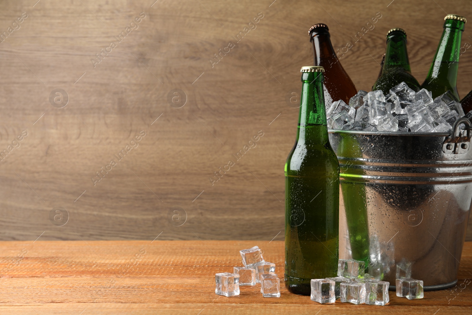 Photo of Metal bucket with beer and ice cubes on wooden background. Space for text