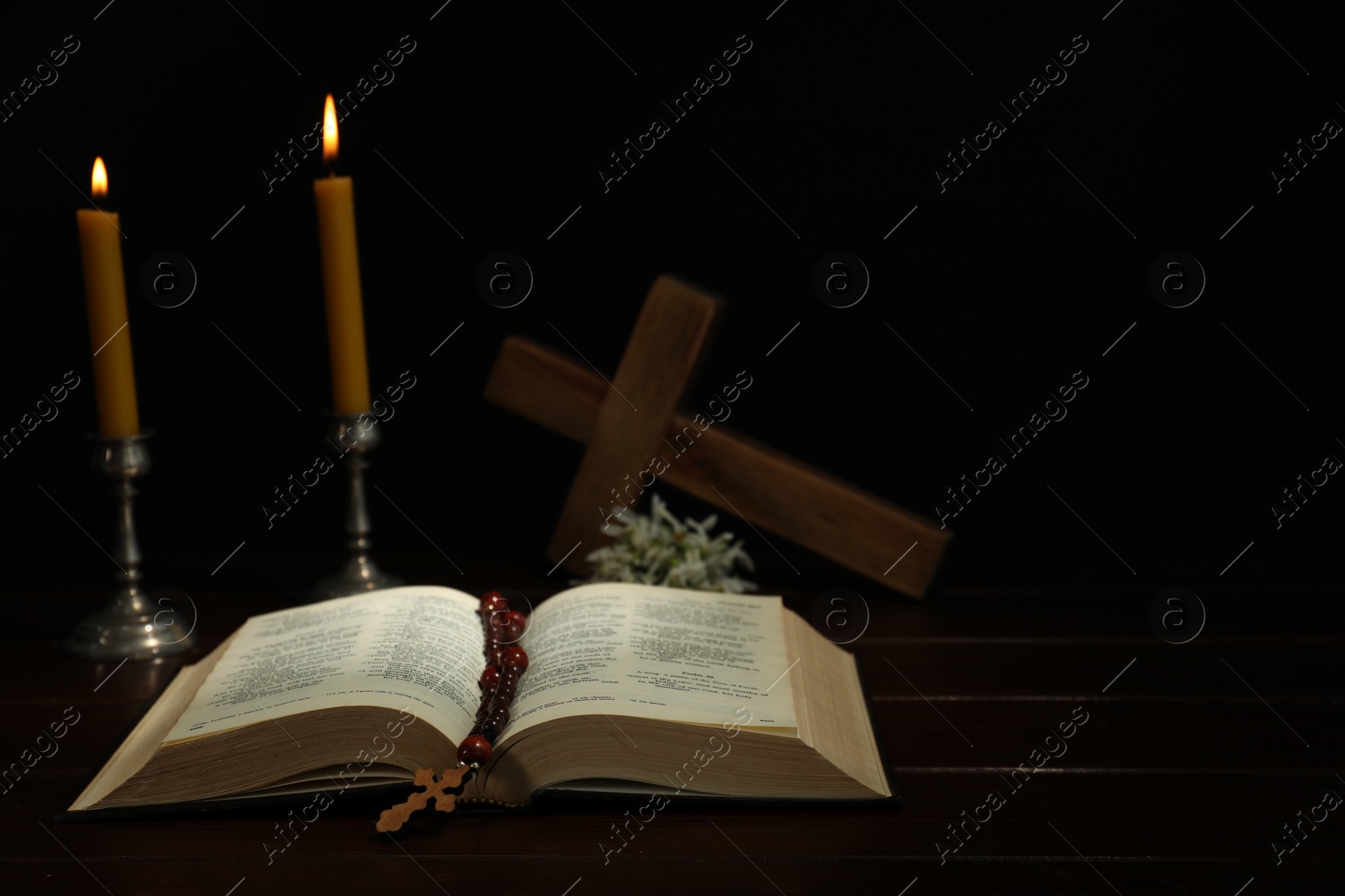 Photo of Crosses, rosary beads, Bible and church candles on wooden table