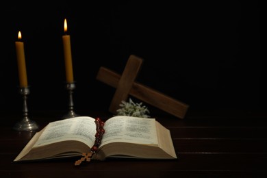 Photo of Crosses, rosary beads, Bible and church candles on wooden table