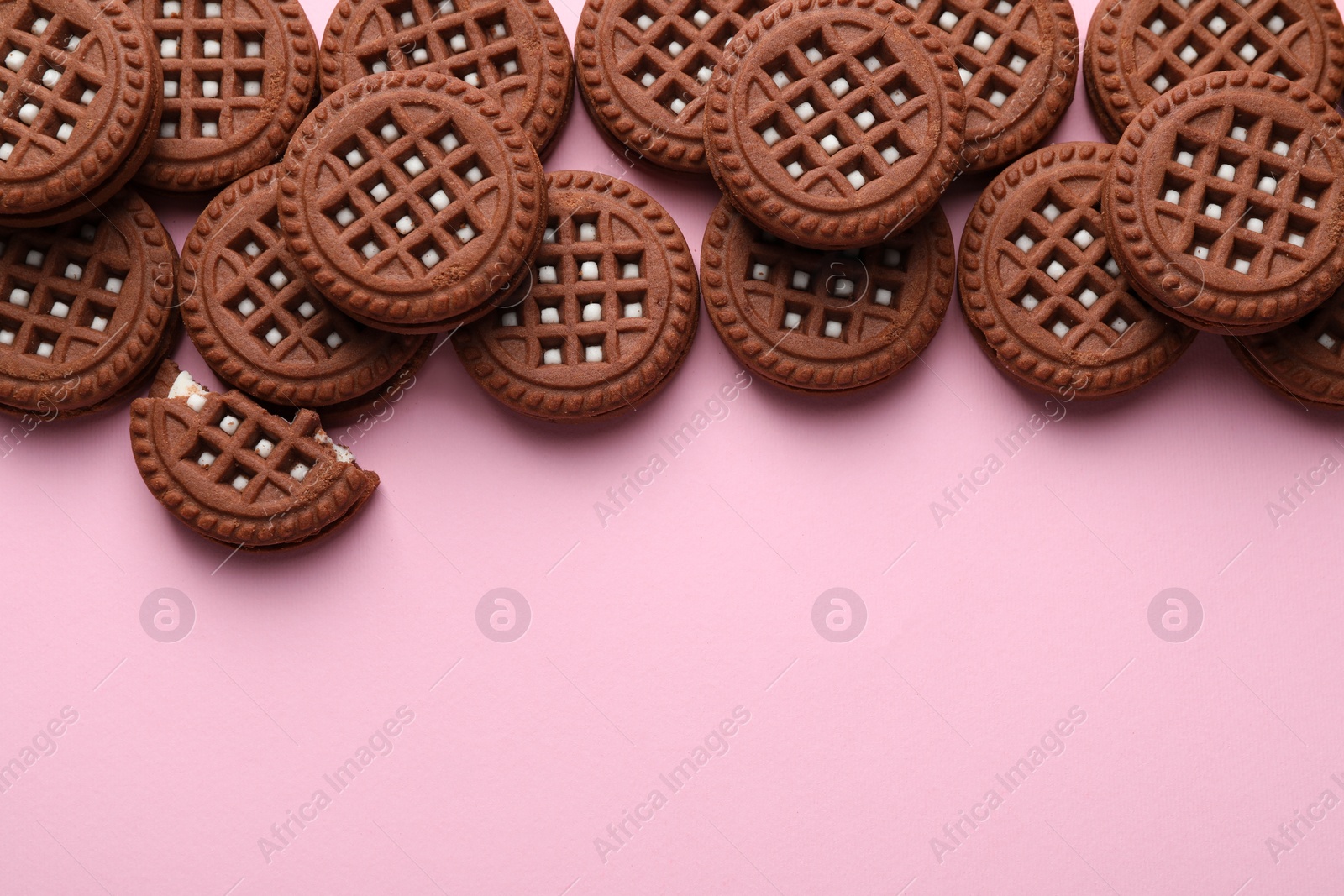 Photo of Tasty chocolate sandwich cookies with cream on pink background, flat lay. Space for text