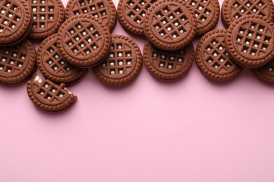 Tasty chocolate sandwich cookies with cream on pink background, flat lay. Space for text